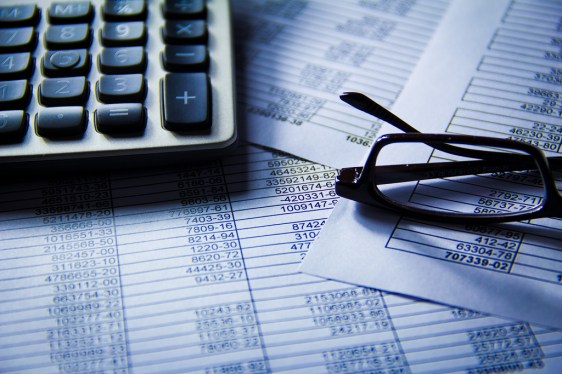 Calculator and glasses on top of spreadsheets full of numbers.