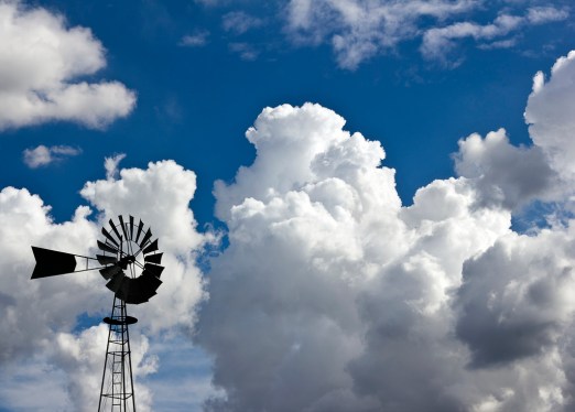 Windmill in front of huge white fluffy clouds against an incredibly blue sky.