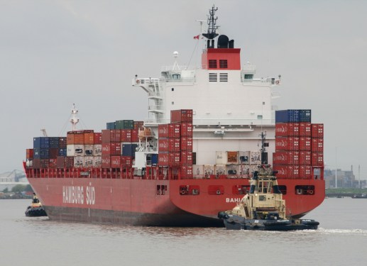 Ship full of containers being pulled into harbor.