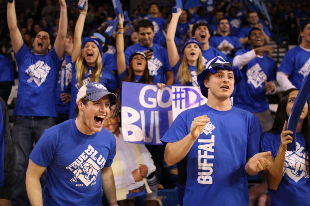 College sports fans all dressed in team color (blue) cheering wildly.