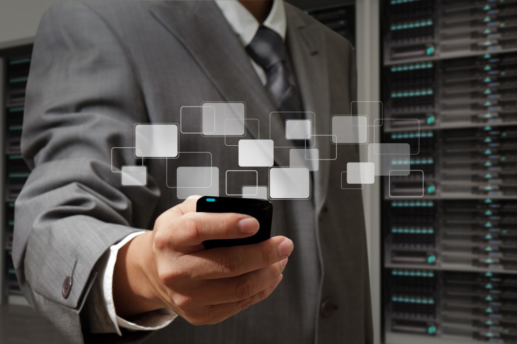 Man holding mobile phone in front of bank of servers.