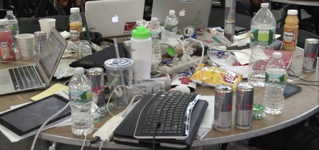 Hackathon table strewn with computers and drinks.