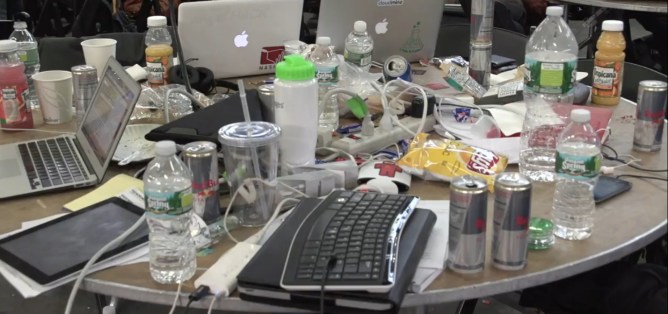 Hackathon table strewn with computers and drinks.