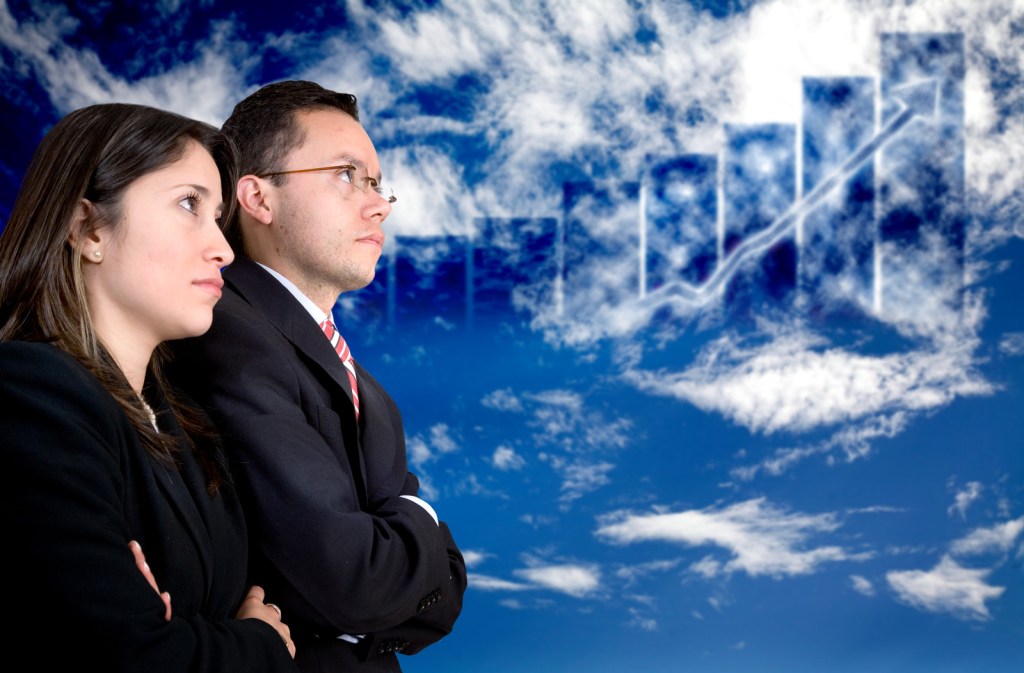 Business people standing in front of graph superimposed over clouds.