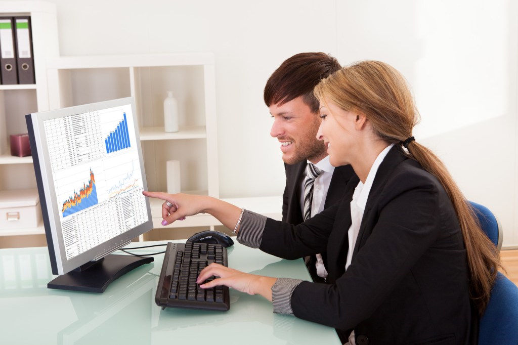 Man and woman in front computer looking at charts and graphs.