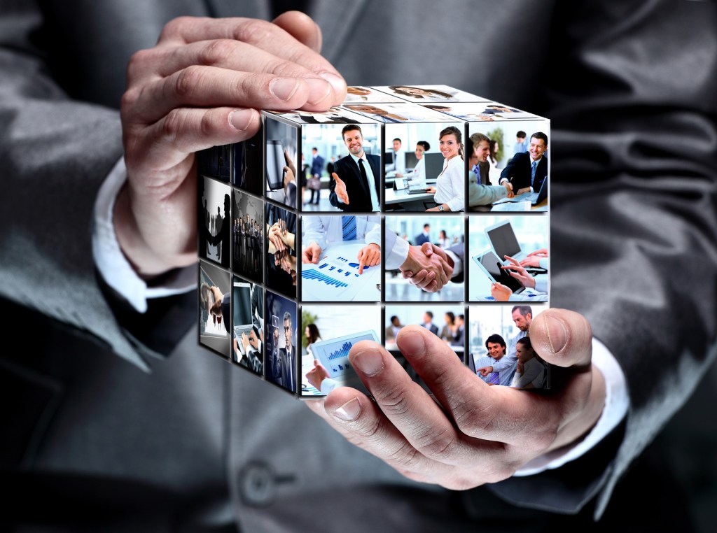 Business man holding a cube with different business images super imposed on it.