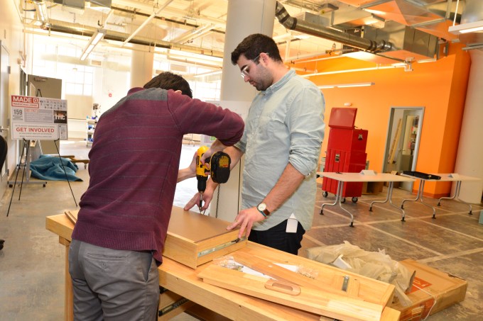Two men building a prototype out of wood using a drill.