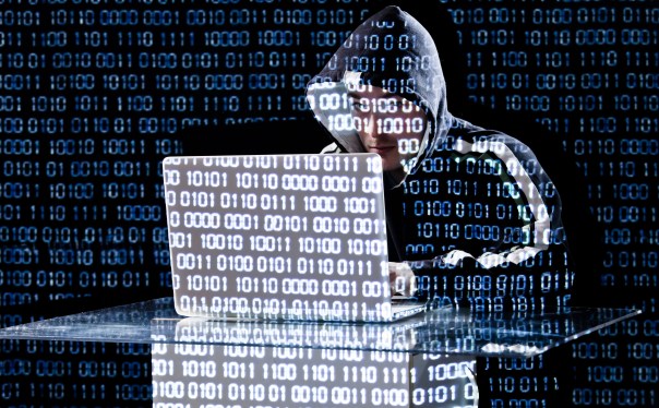 Hacker in hoodie working on PC over background of zeros and ones.