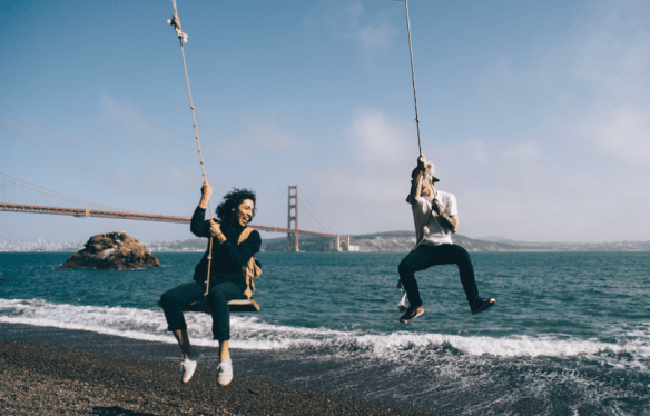 two people swinging at beach with Golden Gate Bridge in the background