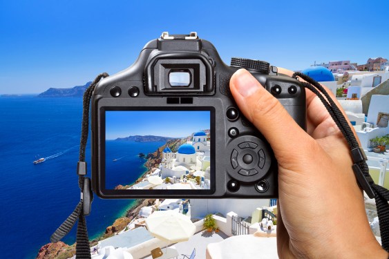 View of a hand holding a digital camera as it aims to take a photo of a coastal enclave