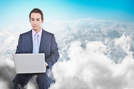 Business man sitting on cloud with laptop in hand.