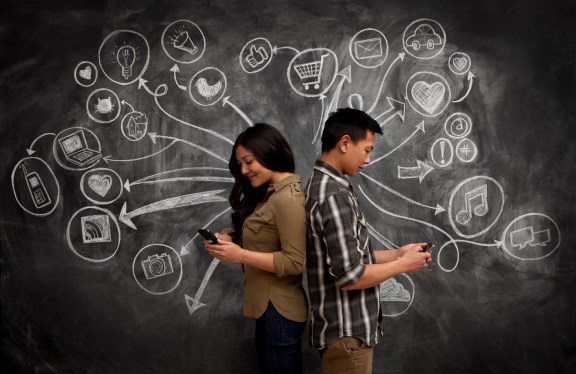 Man and woman back to back with smart phones. Behind them on chalk board is a collection symbols representing different apps.