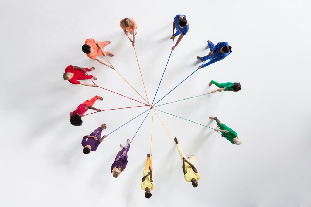 Overhead shot of a small group of people, wearing monochromatic colors, pulling at ropes from opposing directions