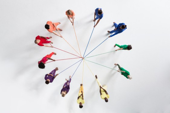 Overhead shot of a small group of people, wearing monochromatic colors, pulling at ropes from opposing directions