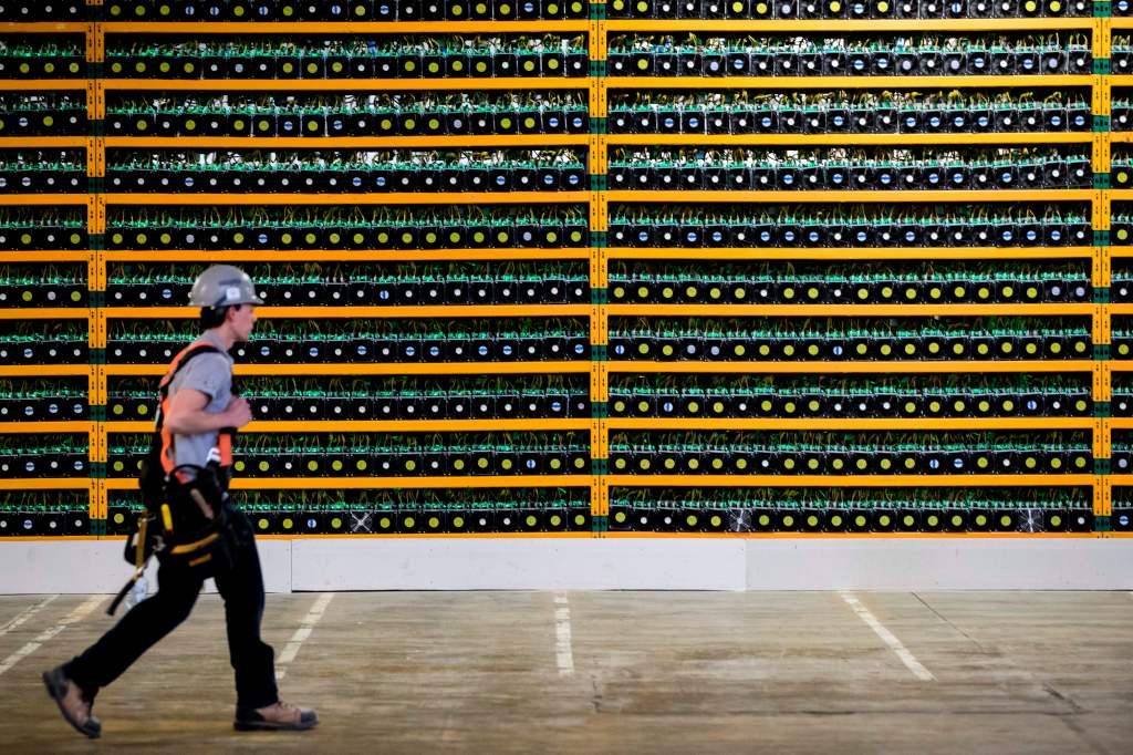Image of a person walking past a wall of bitcoin mining rigs