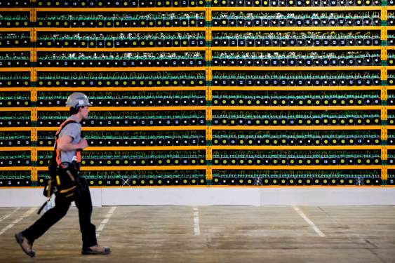 Image of a person walking past a wall of bitcoin mining rigs