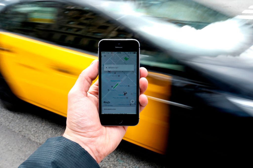 A taxi drives by a phone displaying the Uber app