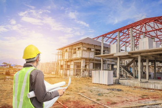 Worker wearing hard hat looking over plans and a construction site.