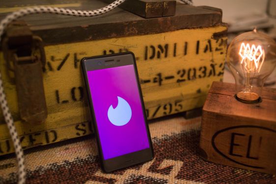 Phone displaying Tinder logo in a still life with crate and Edison light bulb