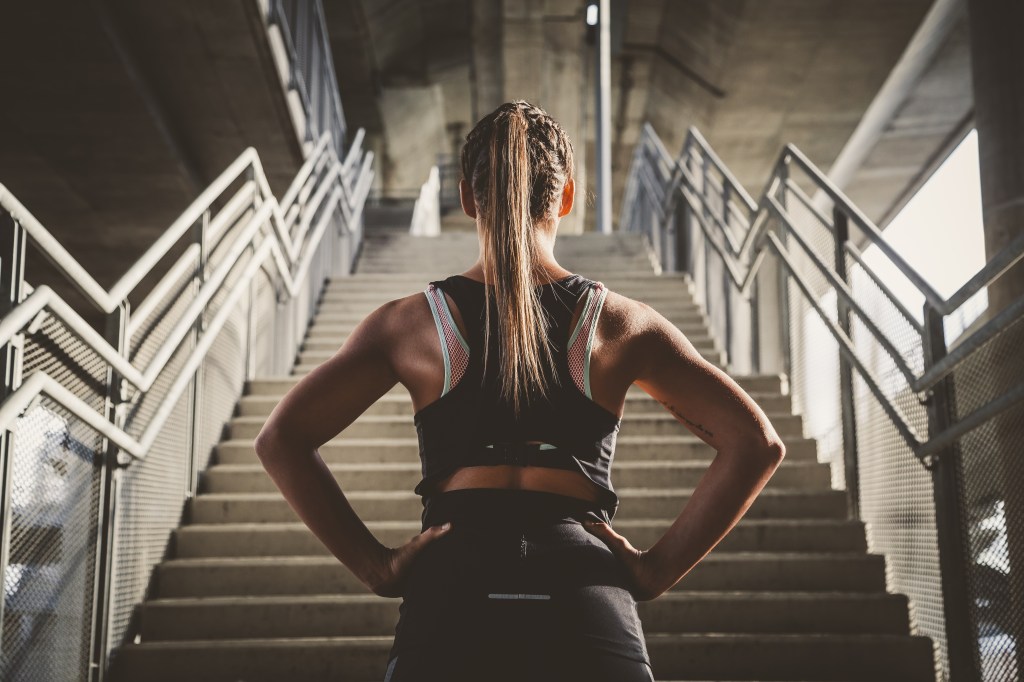 young woman facing flight of stairs ready run up