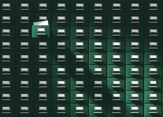 An immense card catalog system with one drawer pulled out, revealing a blank catalog card. This vintage database is floodlighted from the upper left side, giving it a mysterious edge.