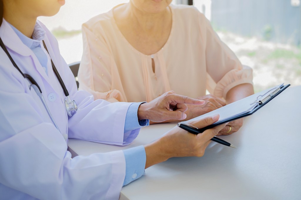 Female Doctor Showing Clipboard To Patient In Hospital