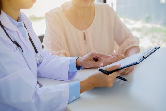 Female Doctor Showing Clipboard To Patient In Hospital