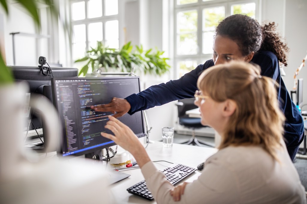 Businesswoman discussing with female colleague over coding on computer at desk in creative office