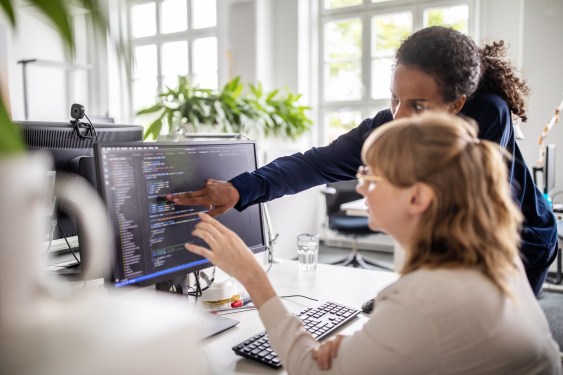Businesswoman discussing with female colleague over coding on computer at desk in creative office
