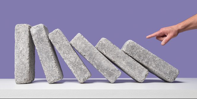 Man's hand point index finger initiating domino effect with 6 concrete blocks on white surface, purple background