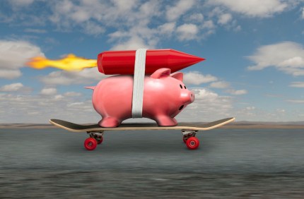A piggy bank streaks down the road to riches on a skateboard and with a rocket strapped to his back.