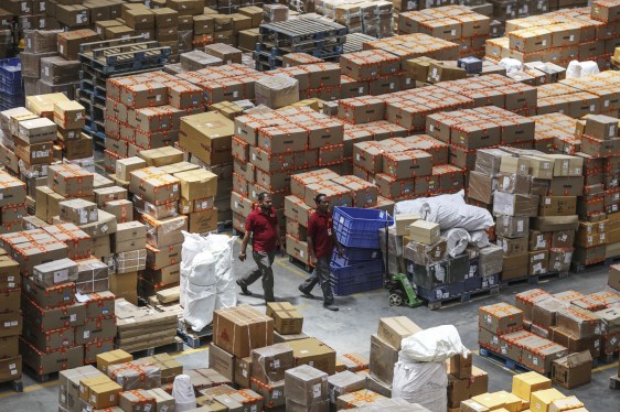 Employees walk past boxes stacked on pallets at a warehouse