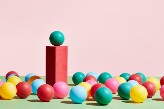 A green sphere stands on top of a pedestal surrounded by a crowd of multicoloured spheres