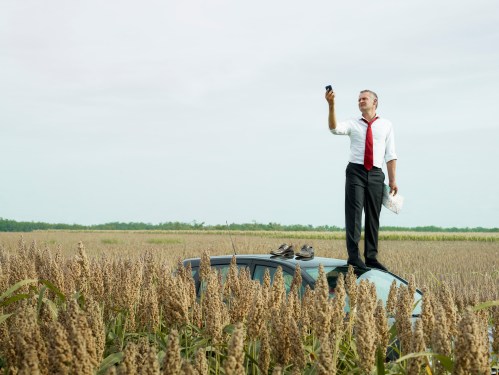 man on top of car in field looking at gps device