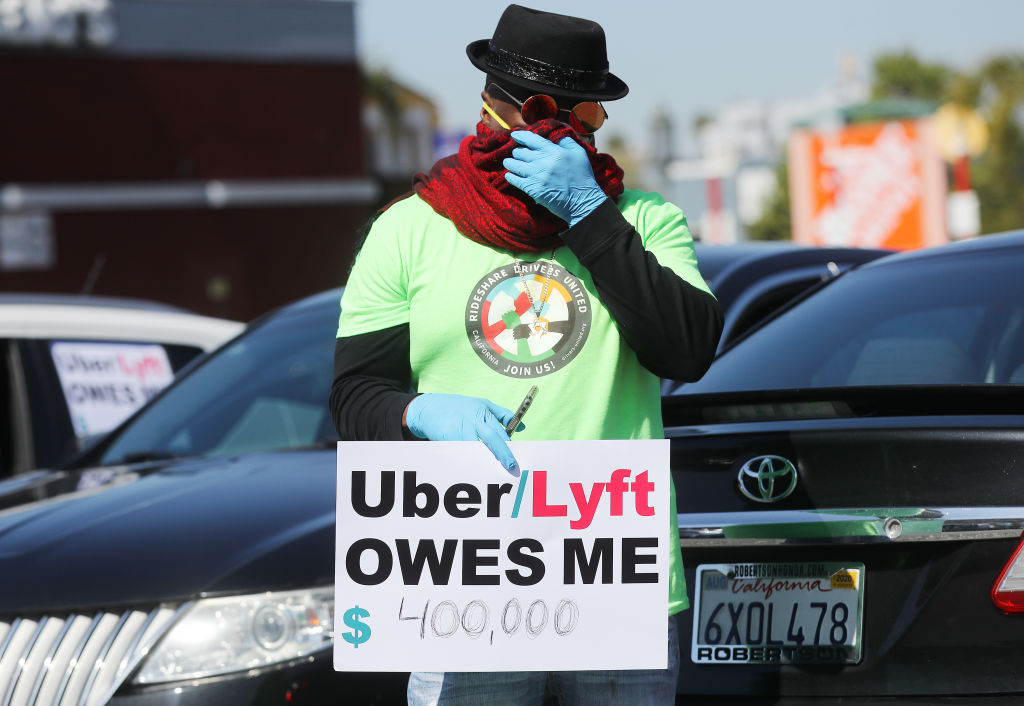 LOS ANGELES, CALIFORNIA - APRIL 16: A protestor displays a sign as Uber and Lyft drivers with Rideshare Drivers United and the  Transport Workers Union of America prepare to conduct a ‘caravan protest’ outside the California Labor Commissioner’s office amidst the coronavirus pandemic on April 16, 2020 in Los Angeles, California. The drivers called for California to enforce the AB 5 law so that they may qualify for unemployment insurance as the spread of COVID-19 continues. Drivers also called for receiving back wages they say they are owed. (Photo by Mario Tama/Getty Images)