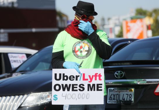 LOS ANGELES, CALIFORNIA - APRIL 16: A protestor displays a sign as Uber and Lyft drivers with Rideshare Drivers United and the  Transport Workers Union of America prepare to conduct a ‘caravan protest’ outside the California Labor Commissioner’s office amidst the coronavirus pandemic on April 16, 2020 in Los Angeles, California. The drivers called for California to enforce the AB 5 law so that they may qualify for unemployment insurance as the spread of COVID-19 continues. Drivers also called for receiving back wages they say they are owed. (Photo by Mario Tama/Getty Images)