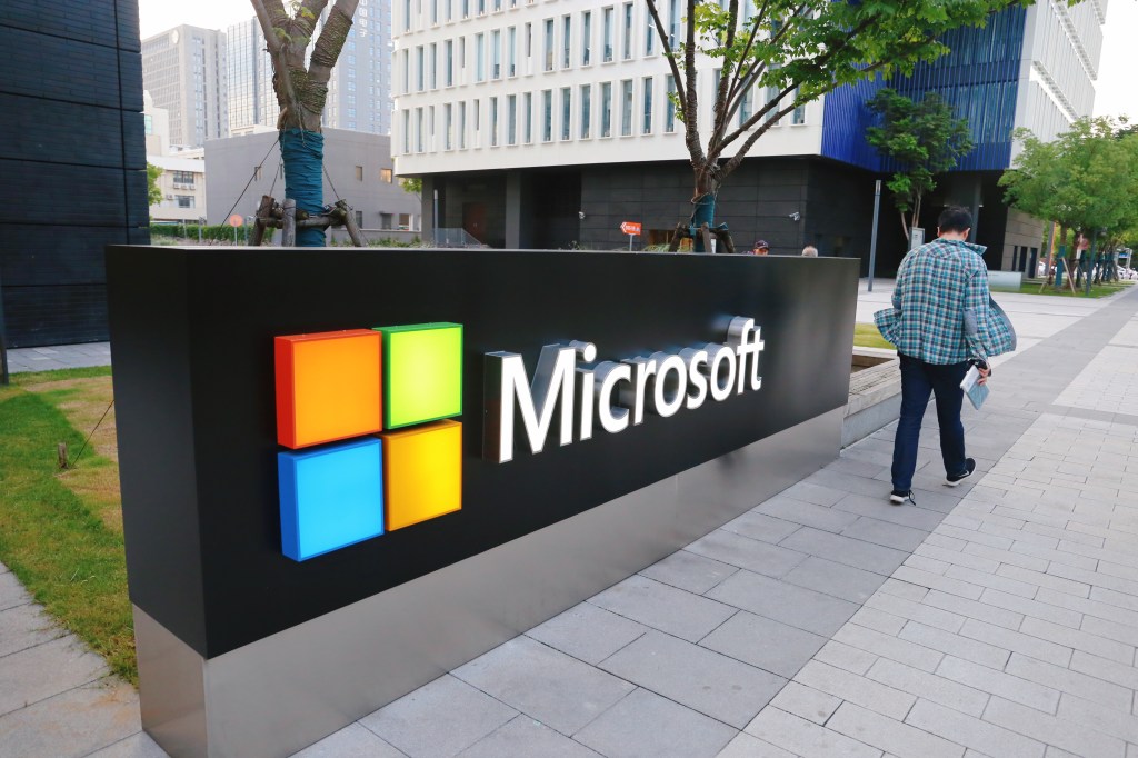 A man walks past a logo of Microsoft outside an office building at Shanghai Caohejing Hi-Tech Park