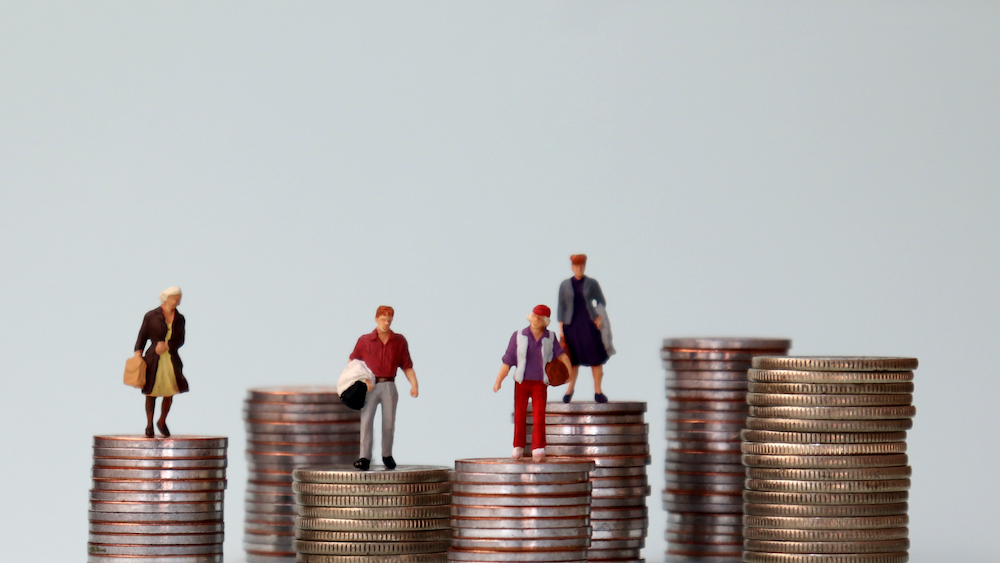 Miniature people standing on piles of different heights of coins. The idea of a growing income gap between individuals.