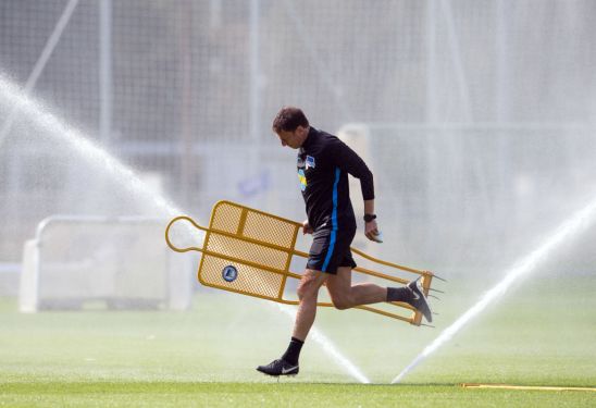 21 July 2019, Berlin: Harald Gämperle, assistant coach of the Bundesliga soccer team Hertha BSC, runs under a sprinkler with a plug-in dummy in his hand across the lawn before training begins. Photo: Soeren Stache/dpa (Photo by Soeren Stache/picture alliance via Getty Images)