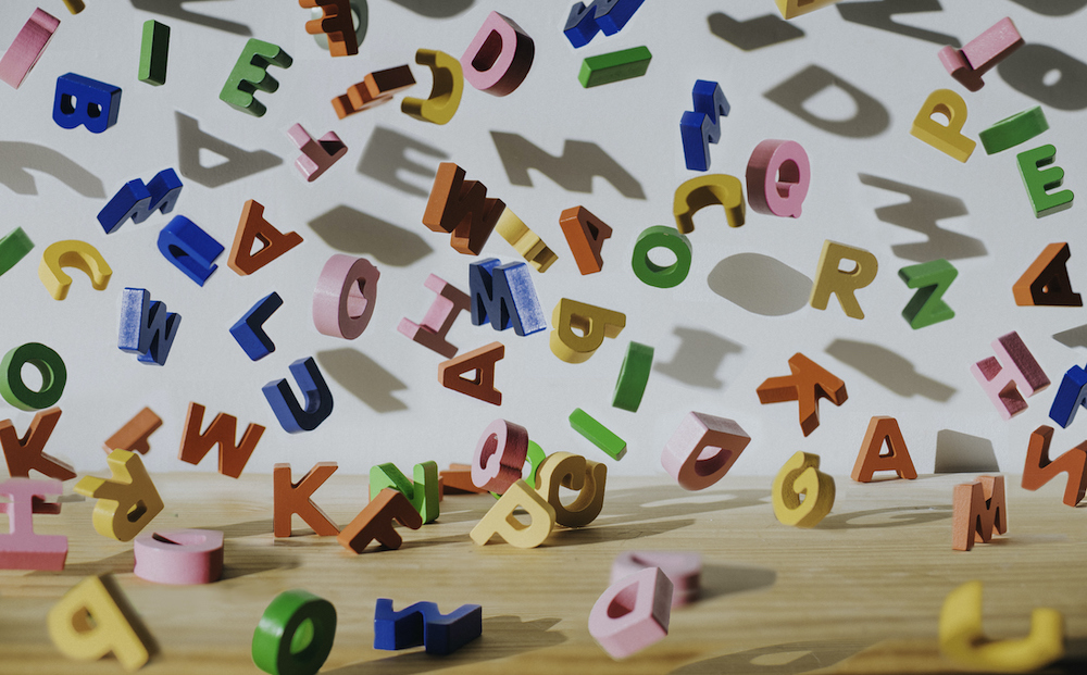 Conceptual image of colourful falling letters, casting shadows on a white wall.