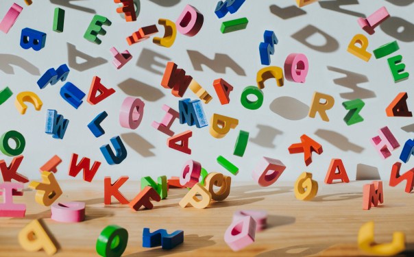 Conceptual image of colourful falling letters, casting shadows on a white wall.