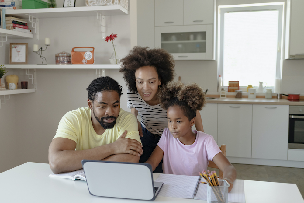 Two African American Parents Helping Their Daughter With Homework while using Laptop in the Kitchen at Home