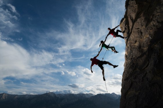 Three rock climbers helping one from falling in a dramatic setting