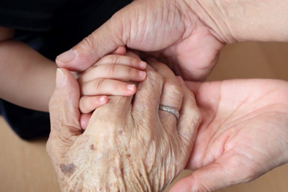 Great grandmother, grandparent and baby putting their hands together