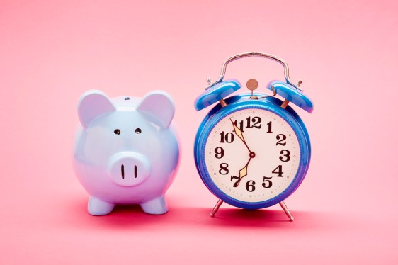 Retro alarm clock and blue piggy bank on pink background