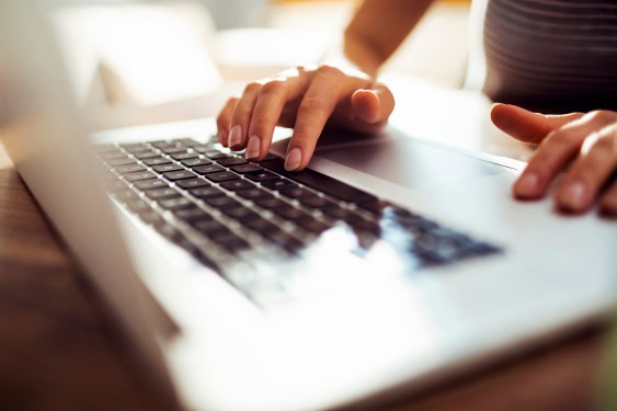 Close up of young woman's hands working on an Apple computer at home.