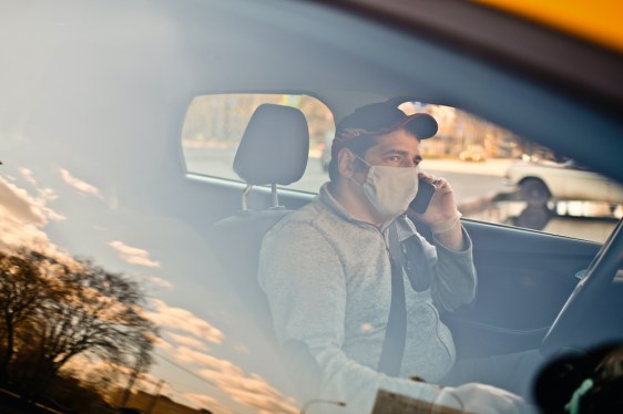 Taxi driver wearing protective medical mask parked on a city street and uses smartphone during an illness epidemic