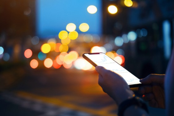 Close up of hands checking financial trading data on smartphone in city street at night