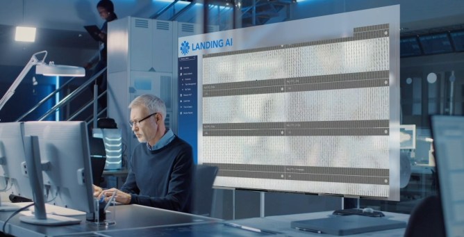 Man working at computer with Landing AI system running data behind him on a large screen.