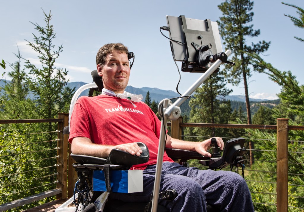 Steve Gleason sits in his wheelchair outside with a monitor mounted on it.